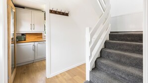 Una cocina con gabinetes blancos, encimera de madera y una escalera con peldaños alfombrados de color gris.