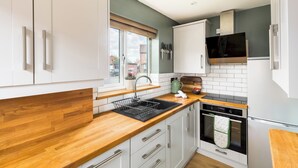 Una cocina moderna con armarios blancos, encimera de madera, horno empotrado y campana extractora de acero inoxidable.