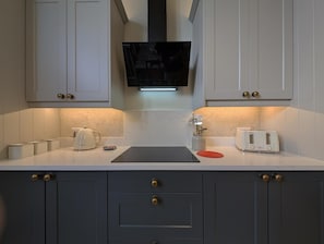 Eine Küche mit weißen Schränken, einer schwarzen Arbeitsplatte, einem Toaster, einem Wasserkocher und einem an der Wand montierten Fernseher.