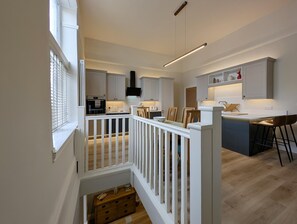 A modern kitchen with white cabinetry, a central island, and a dining area with bar stools. - Cullercoats Coastal Escape - 3 bedroom Modern Home - Pass the Keys (Newcastle)