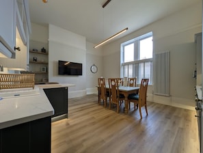 Eine moderne Küche mit Essbereich, Holzkstühlen, einem Fernseher und einer Uhr an der Wand.