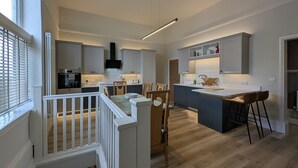 A modern kitchen with a central island, wooden flooring, and a dining area with chairs. - Cullercoats Coastal Escape - 3 bedroom Modern Home - Pass the Keys (Newcastle)