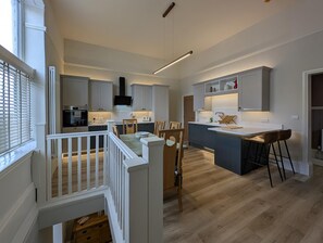 A modern kitchen with a central island, wooden flooring, and a dining area with chairs. - Cullercoats Coastal Escape - 3 bedroom Modern Home - Pass the Keys (Newcastle)