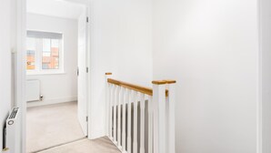 Um corredor branco com corrimão de madeira, radiador e janela com vista para edifícios.
