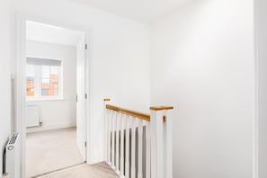 A white hallway with a wooden handrail, a radiator, and a window with a view of buildings. - 2 Bed Modern Terrace, Leamington Spa - Pass the Keys (Leamington Spa)
