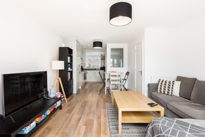 A modern living room with a TV, a wooden coffee table, a sofa, and a kitchen in the background. - 2 Bed Modern Terrace, Leamington Spa - Pass the Keys (Leamington Spa)