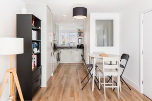 A modern kitchen with white cabinets, a dining table with chairs, a lamp, and a bookshelf. - 2 Bed Modern Terrace, Leamington Spa - Pass the Keys (Leamington Spa)