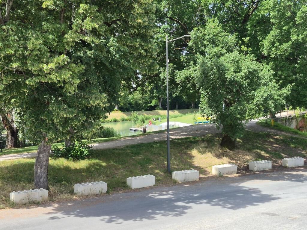 Una carretera pavimentada con bolardos blancos, una zona verde y árboles.