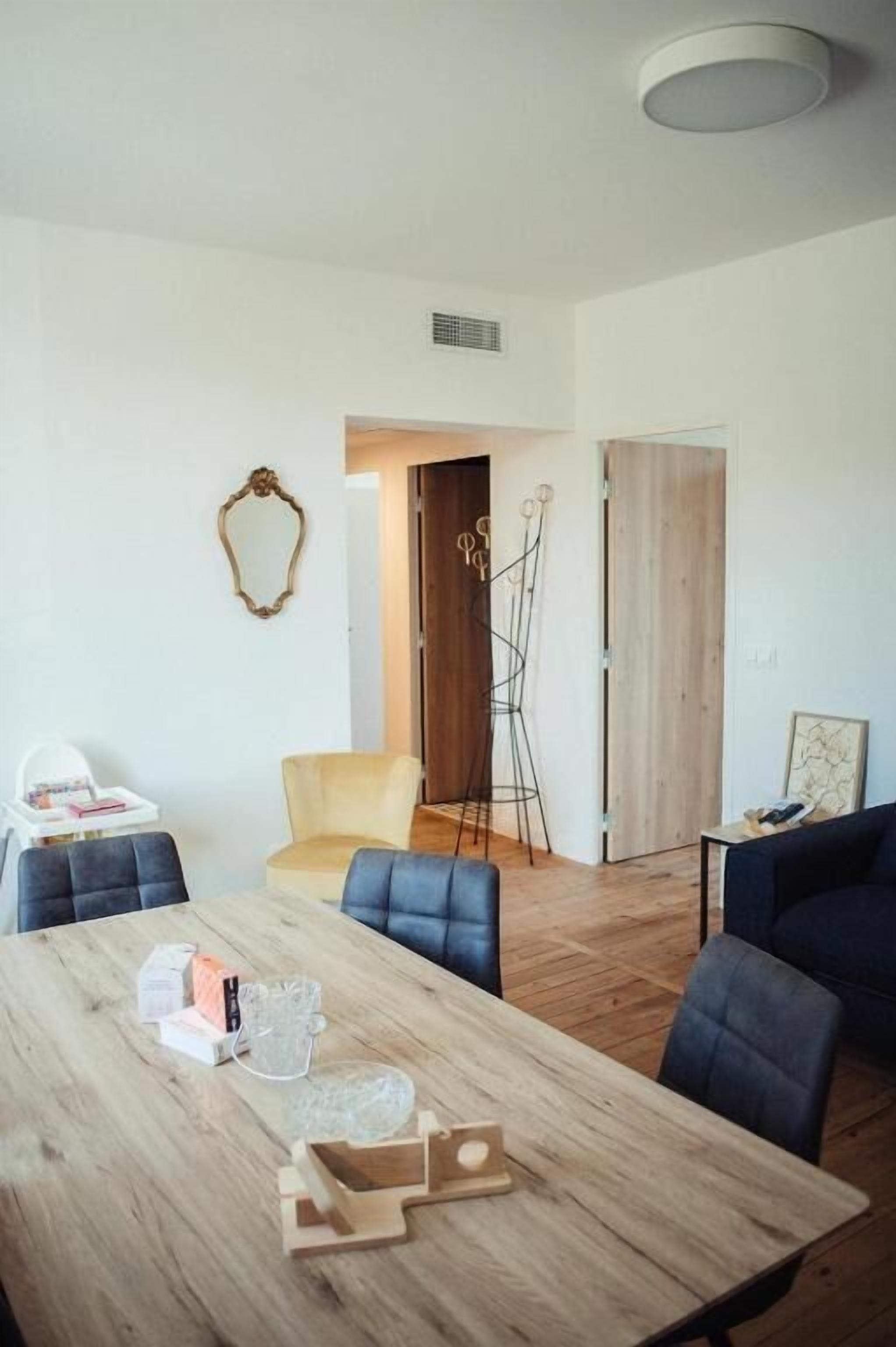 Una sala de estar moderna con una mesa de comedor de madera, sillas azules, un sillón amarillo y un sofá oscuro.