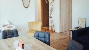 A modern living room with a wooden dining table, blue chairs, a yellow armchair, and a dark sofa. - Les Logis du Port Canal Suites & Spas  (Montauban)
