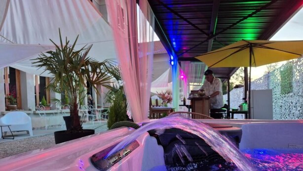 A hot tub with water jets, a person working at a bar, and a tented outdoor area with plants. - Les Logis du Port Canal Suites & Spas  (Montauban)