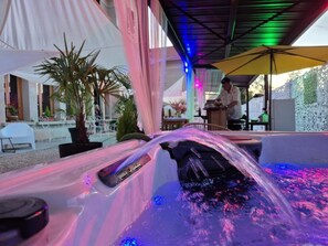 A hot tub with water jets, a person working at a bar, and a tented outdoor area with plants.