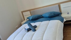 A neatly made bed with a white comforter and blue pillows, a small bedside table with a lamp, and a water bottle on it. - Les Logis du Port Canal Suites & Spas  (Montauban)