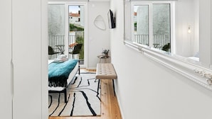 Un pasillo estrecho con una cama, una mesita y una silla, que da a un balcón con vistas.