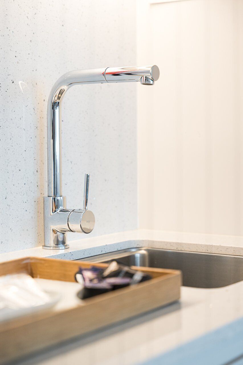 A modern kitchen with a stainless steel sink, a wooden tray, and a chrome faucet.