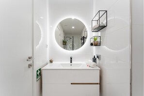 Une salle de bain moderne avec un miroir rond, un lavabo blanc et une cabine de douche en verre.
