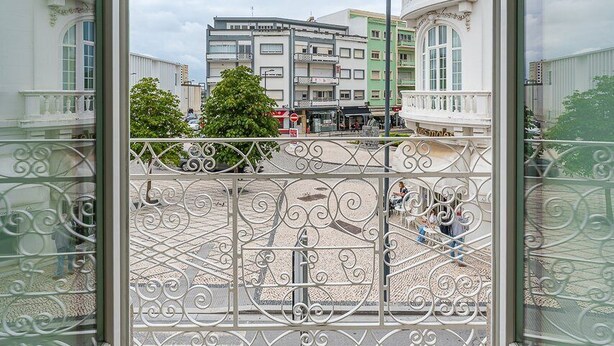 Vista desde un balcón con barandillas de metal ornamentadas, un edificio de arquitectura clásica y cielo despejado.