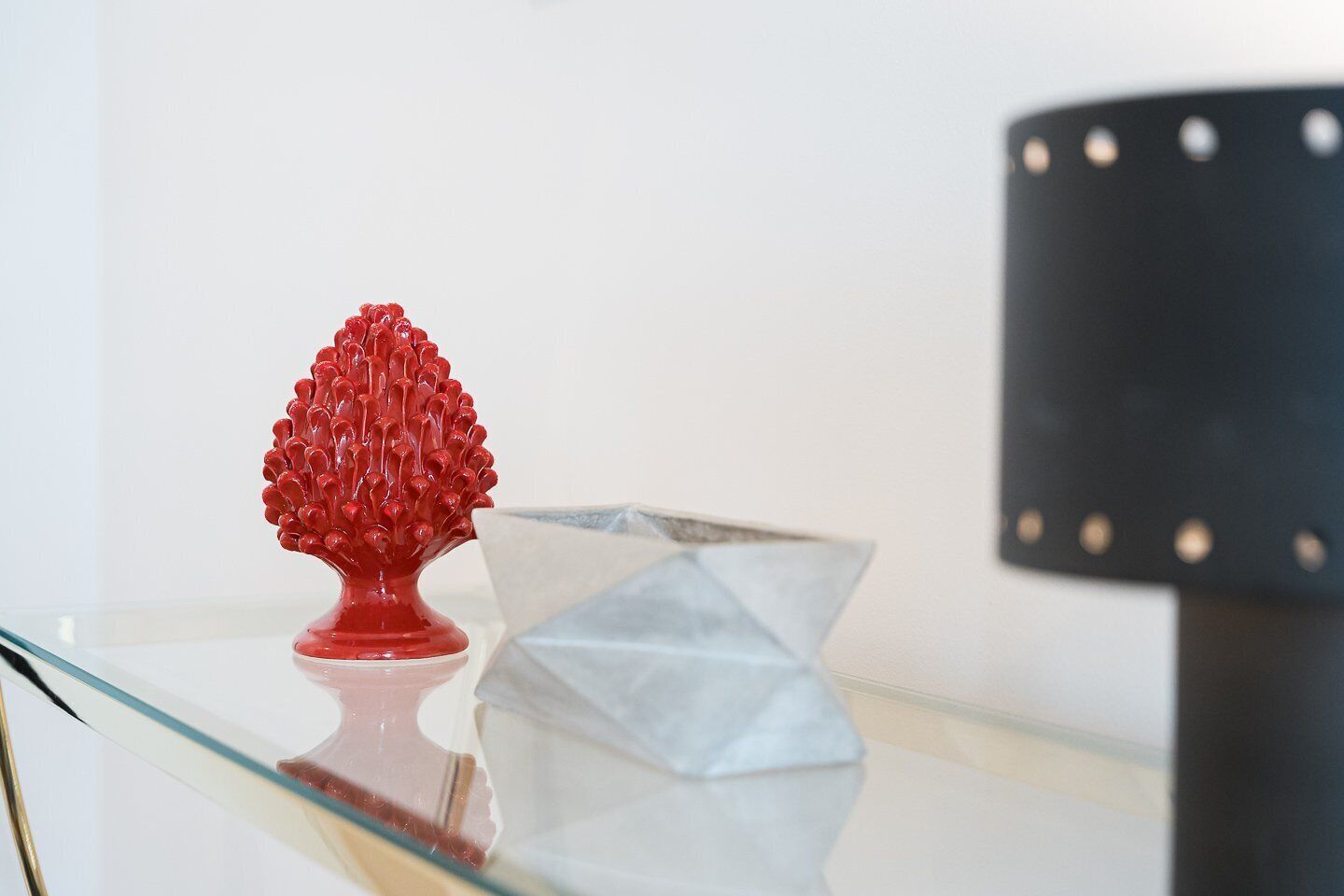 Una mesa de vidrio con un objeto esférico rojo y una escultura de papel blanco.