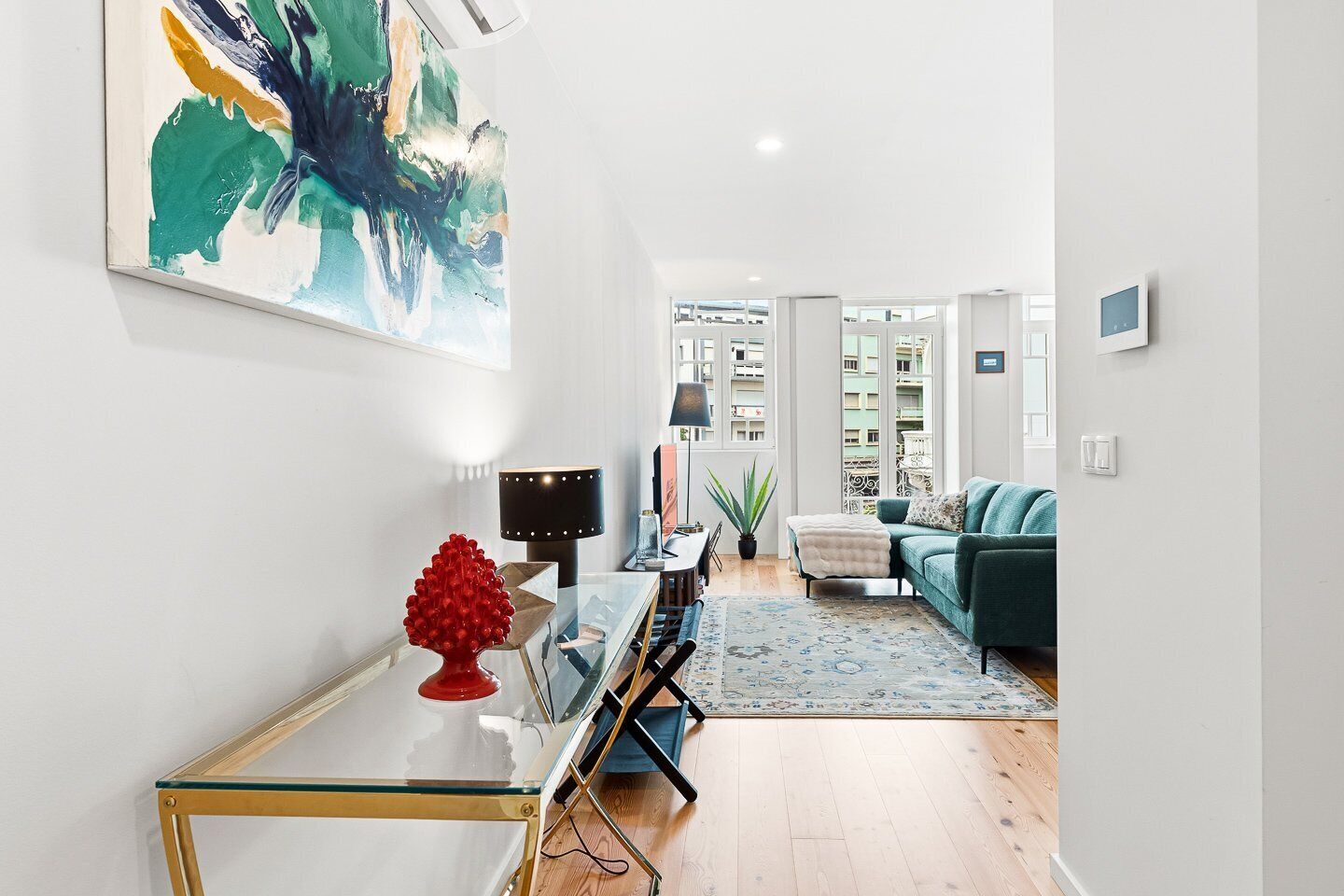 Un salon moderne avec une table basse en verre, un objet décoratif rouge, un canapé turquoise et un grand tableau abstrait accroché au mur.