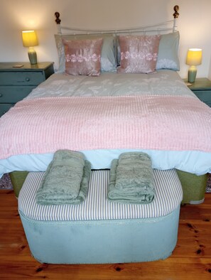 A neatly made bed with a pink blanket, two pillows, and a green towel on an ottoman.