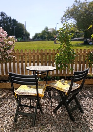 A round table with two chairs, a wooden fence, and a garden in the background.