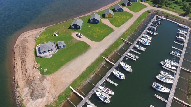 An aerial view of a marina with boats docked, a dirt path, and several small houses with distinct roofs.