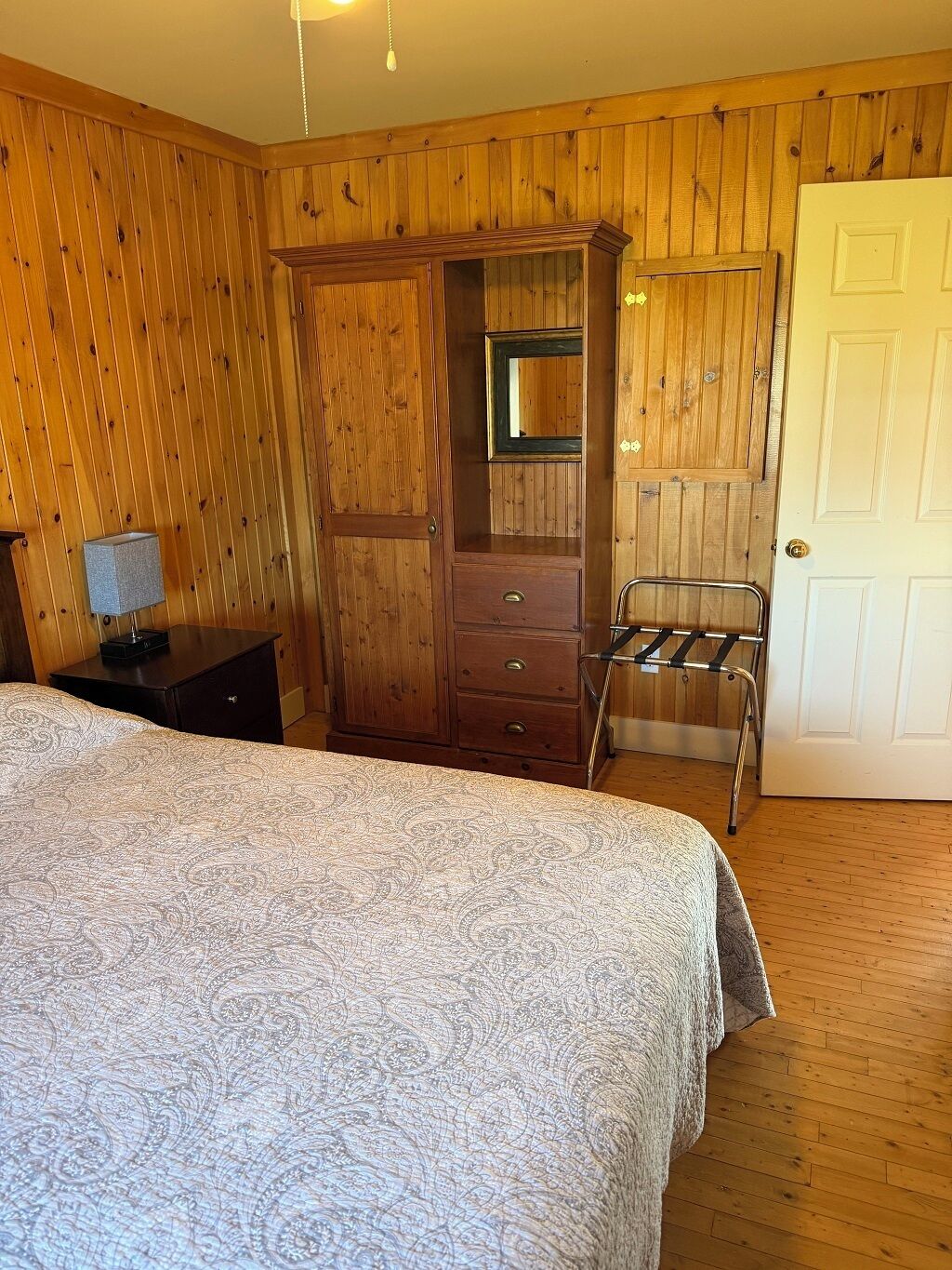 Een kamer met houten lambrisering, een bed, een kledingkast, een spiegel en een deur.
