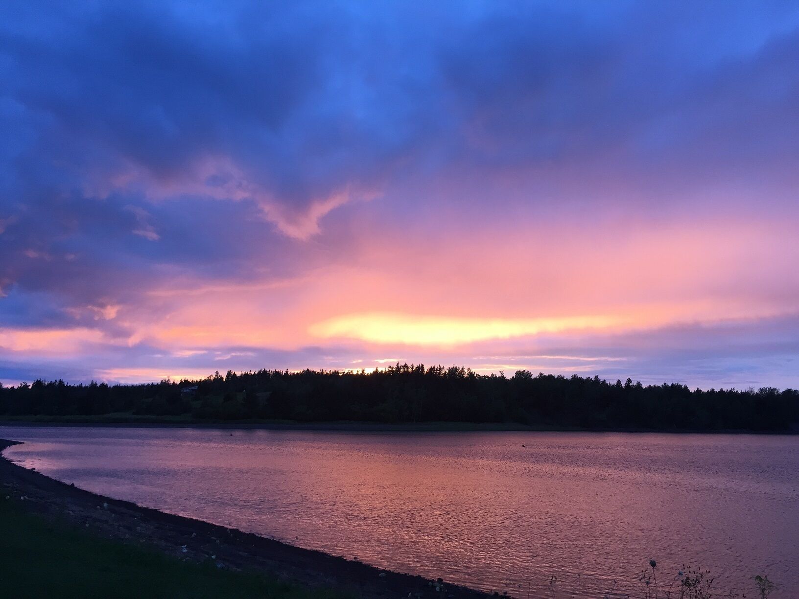 A calm lake at sunset with a forested shoreline.