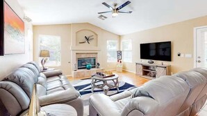 A living room with a fireplace, a television, and a ceiling fan. - Spacious Home in a Central Location w/ Private Pool & Fire Pit (Gilbert)