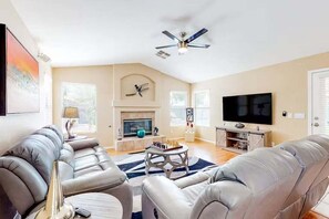 A living room with a fireplace, a television, and a ceiling fan. - Spacious Home in a Central Location w/ Private Pool & Fire Pit (Gilbert)