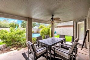 A covered patio with a dining table and chairs, a ceiling fan, and a view of a swimming pool. - Spacious Home in a Central Location w/ Private Pool & Fire Pit (Gilbert)