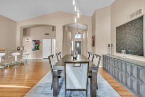 A spacious dining area with a long table, chairs, and a decorative wall. - Spacious Home in a Central Location w/ Private Pool & Fire Pit (Gilbert)