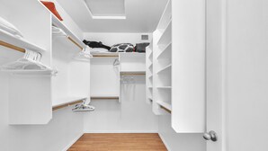 A narrow walk-in closet with wooden flooring, white walls, and shelves for storage. - Spacious Home in a Central Location w/ Private Pool & Fire Pit (Gilbert)