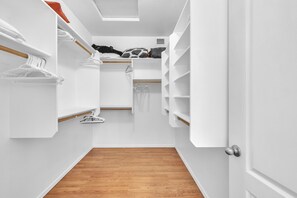 A narrow walk-in closet with wooden flooring, white walls, and shelves for storage. - Spacious Home in a Central Location w/ Private Pool & Fire Pit (Gilbert)