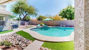 A backyard with a swimming pool, a barbecue grill, and a stone wall. - Spacious Home in a Central Location w/ Private Pool & Fire Pit (Gilbert)