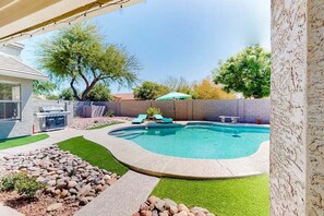 A backyard with a swimming pool, a barbecue grill, and a stone wall. - Spacious Home in a Central Location w/ Private Pool & Fire Pit (Gilbert)