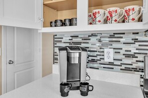 A kitchen with a coffee maker, two black coffee mugs, and a tiled backsplash. - Spacious Home in a Central Location w/ Private Pool & Fire Pit (Gilbert)