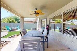 Eine Terrasse im Freien mit Tisch und Stühlen, einem Deckenventilator und Blick auf einen Garten.