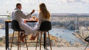A couple dining at a table with a city view. - 24th Floor Sea Front view Apart Hotel Mercury Tower 3 Pools-Cave Spa-Gym-Rooftop (St. Julian's)