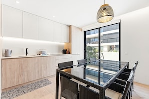 Una cocina moderna con armarios blancos, una mesa de comedor de vidrio, sillas de mimbre y una lámpara colgante.