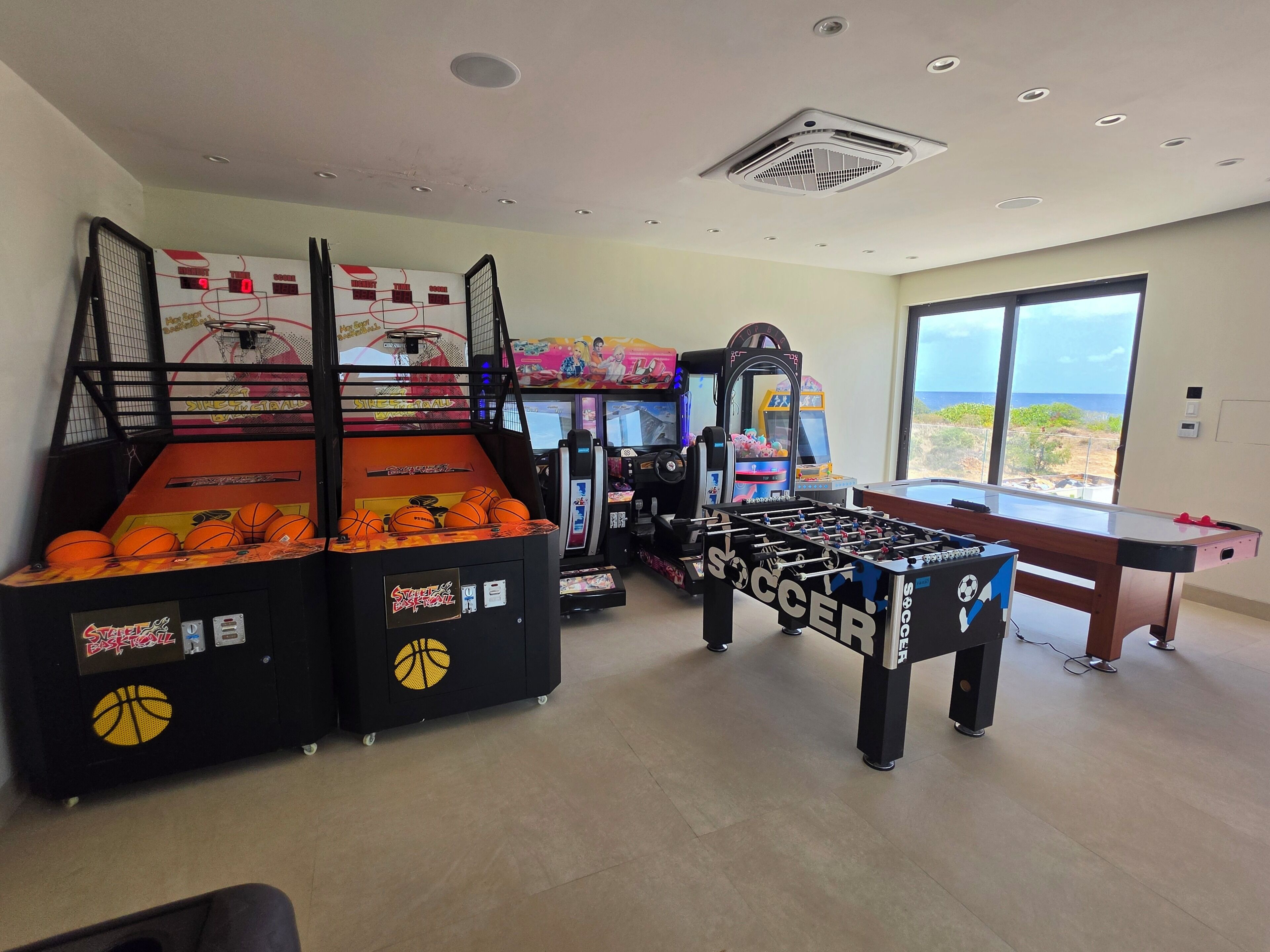 Una habitación con mesa de fútbol, juegos de baloncesto tipo arcade y un ventanal con vistas.