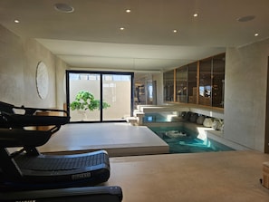 Ein moderner Wellnessbereich mit Massageliege, einem kleinen Pool und Blick ins Freie.