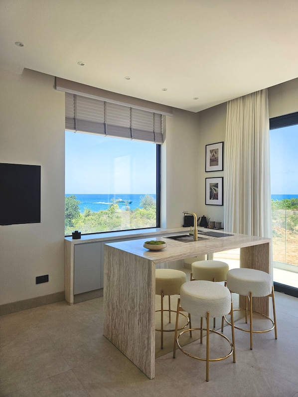 A modern kitchen with a large window, a bar area with stools, and a view of the ocean.