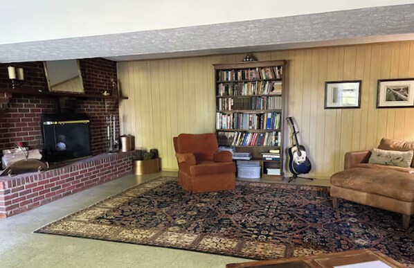 A living room with a fireplace, a bookshelf, a guitar, and a patterned rug.