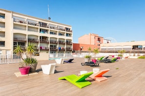A rooftop pool area with lounge chairs, potted plants, and a building with balconies. - LVAM - Duplex Apartment for 4 Guests - In the Heart of Cap d'Agde - Pool (Le Cap D'Agde)