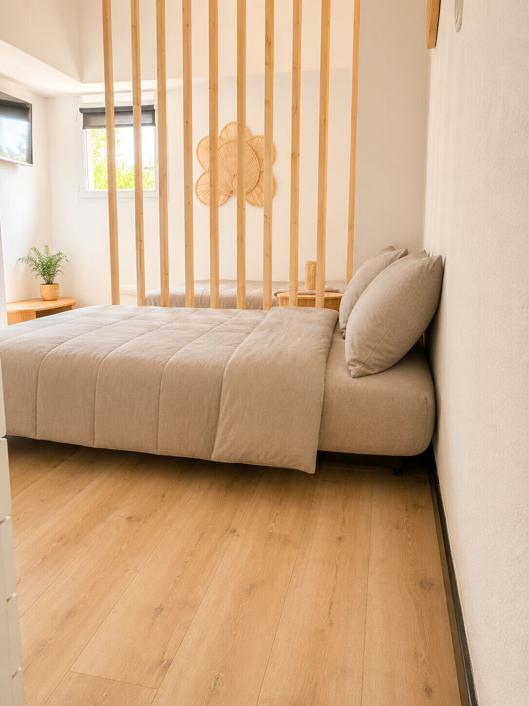 Ein schlicht eingerichtetes Schlafzimmer mit Bett, Holzbalken, einem kleinen Nachttisch und einem Fenster.