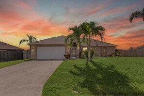 A single-story house with a garage, a well-maintained lawn, and a palm tree. - Game Room! Large Pool + Privacy Fence! (Cape Coral)