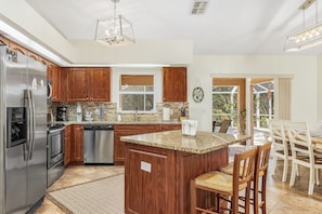 A modern kitchen with wooden cabinets, stainless steel appliances, granite countertops, and a bar area with chairs. - Game Room! Large Pool + Privacy Fence! (Cape Coral)
