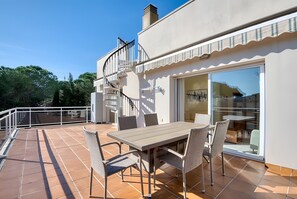 Eine Terrasse mit Tisch und Stühlen, eine Wendeltreppe und eine Glastür zu einem Innenbereich.
