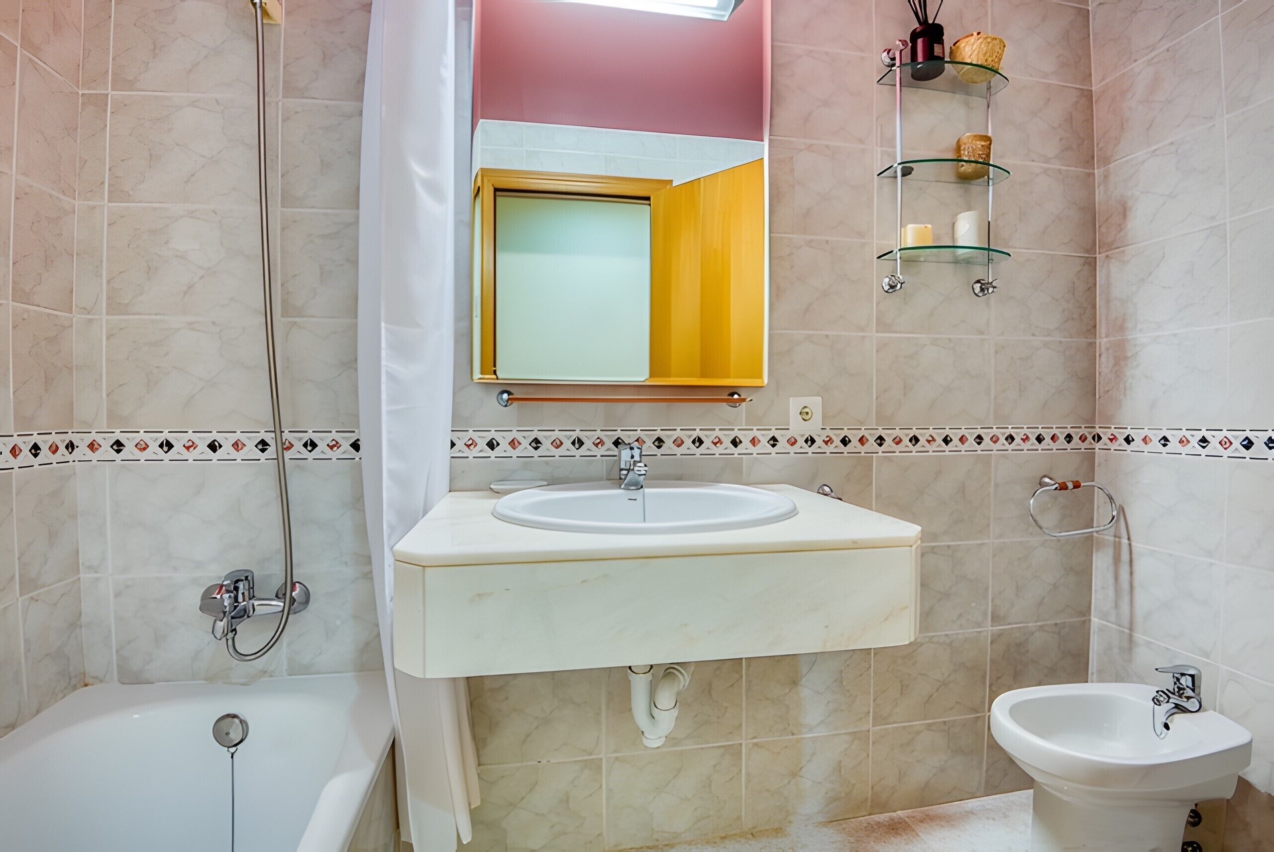 A bathroom with a bathtub, a sink, a bidet, a mirror, and a shelf with toiletries.